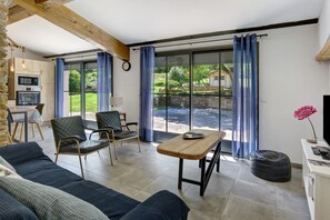 Ein modernes Wohnzimmer mit einer Couch, Sesseln, einem Holztisch und einer Küchenzeile mit einer Mikrowelle.
