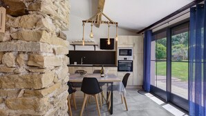 Una cocina moderna con pared de piedra, mesa y sillas de madera, y un amplio ventanal con vistas.