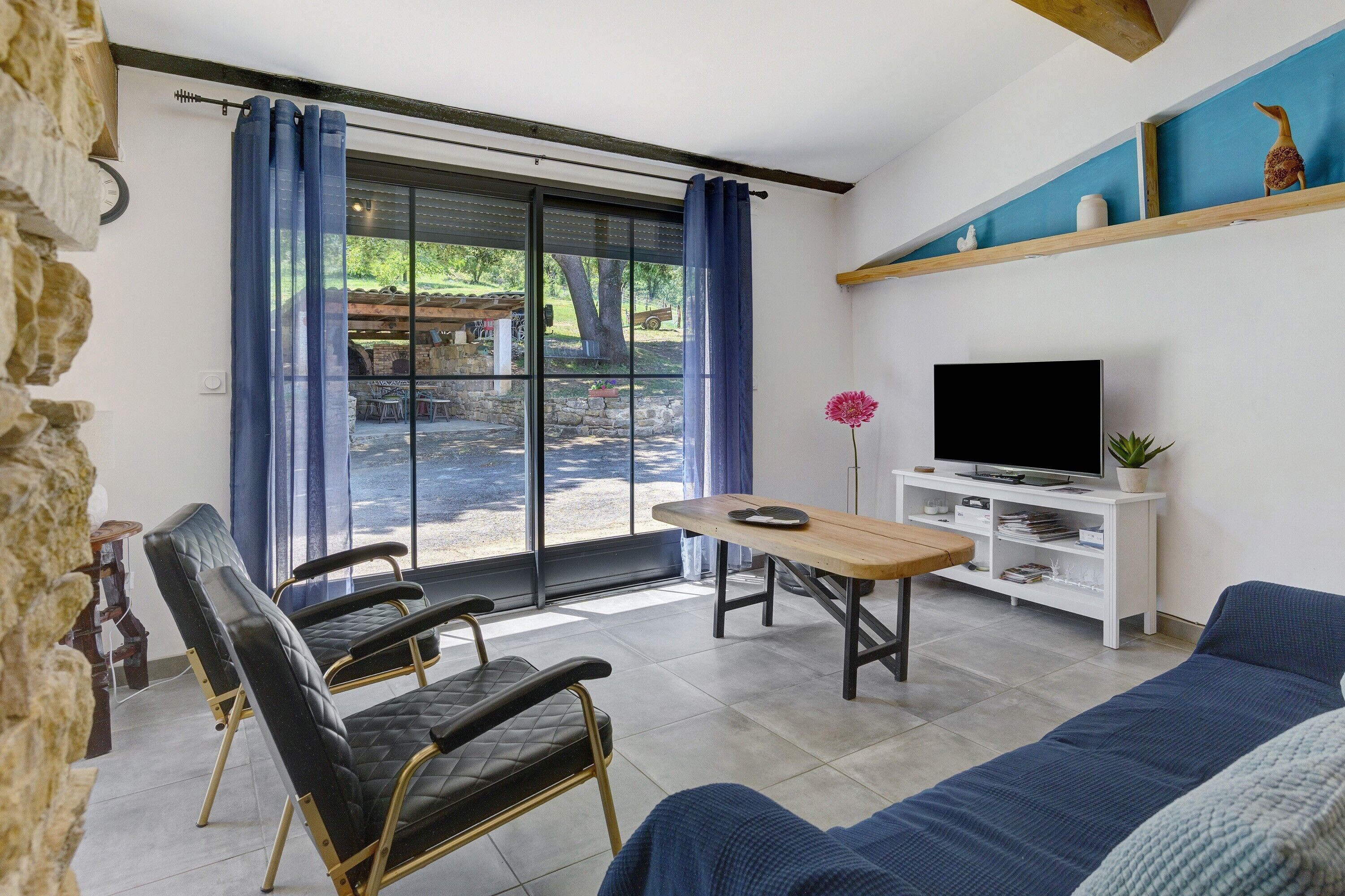 Ein Wohnzimmer mit einer Couch, einem Tisch, einem Fernseher und Blick durch eine Glastür.