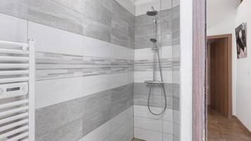 Une douche équipée d’un pommeau de douche à main, d’un porte-serviettes blanc et d’un mur carrelé orné d’un motif géométrique.