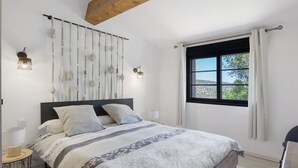 Un dormitorio con cama, lámparas de noche, una ventana con cortinas y vistas al exterior.
