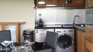 Een compacte keuken met houten kastjes, een roestvrijstalen spoelbak, een wasmachine en een eethoek met een tafel en stoelen.