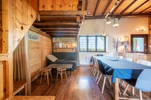 A cozy room with wooden walls, a sofa, a dining table with chairs, and a bookshelf.
