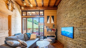A cozy room with a wooden ceiling, a sofa with cushions, a small round table, a bookshelf, and a framed picture on the wall.