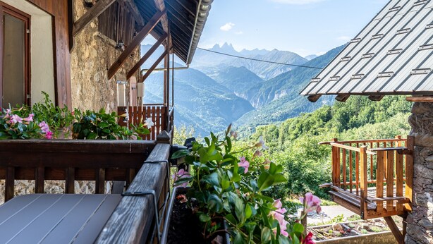 A wooden balcony with a stone wall, a wooden bench, and a view of mountains.