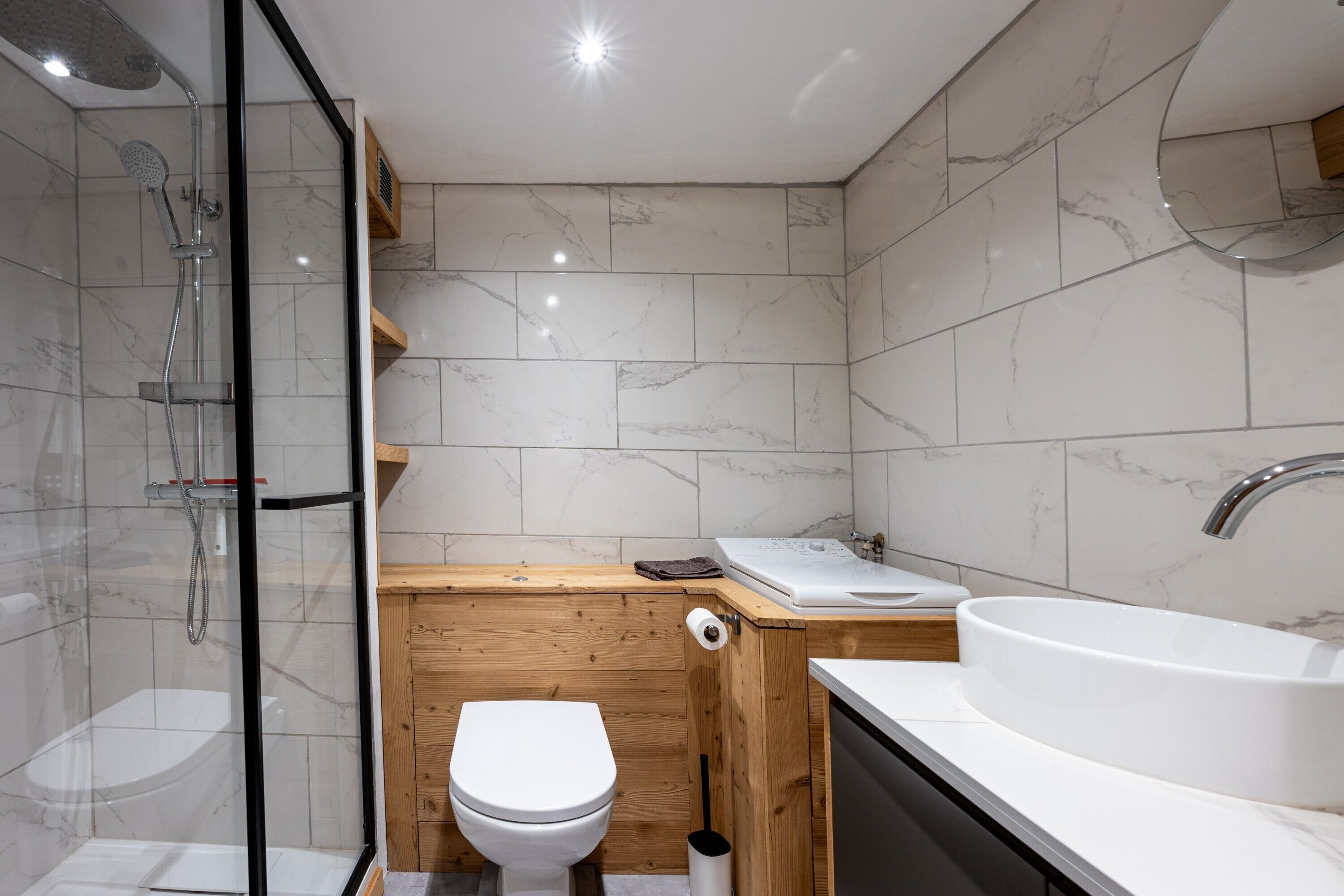 Une salle de bain moderne avec une douche à parois de verre, un meuble-lavabo en bois, un lavabo blanc et des toilettes.