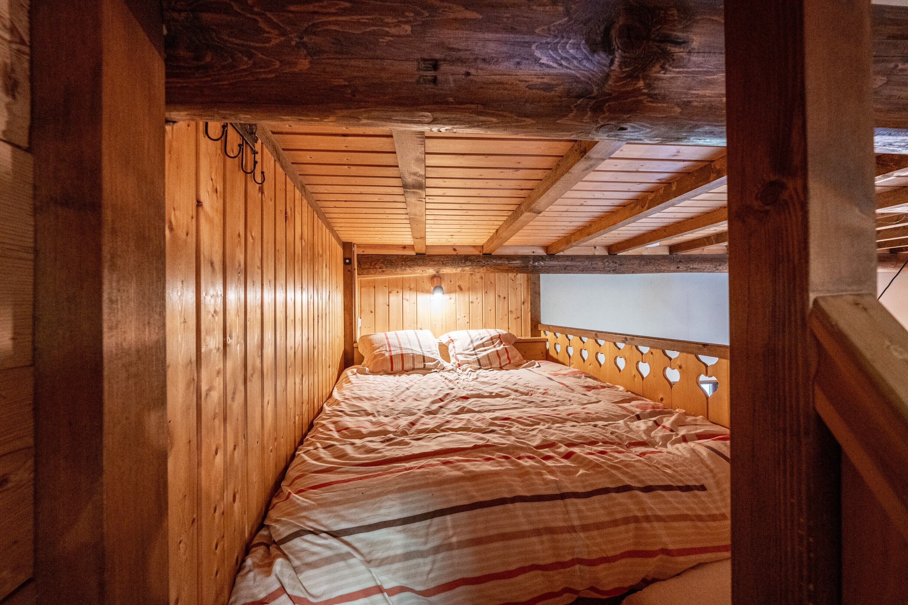 A wooden cabin bedroom with a bed, wooden walls, and a sloped ceiling.
