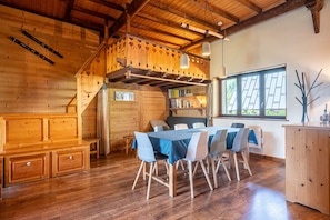A wooden interior with a dining table, chairs, a bench, and a bookshelf.