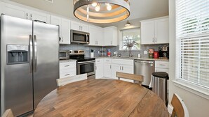 Una cocina moderna con armarios blancos, electrodomésticos de acero inoxidable, una mesa de comedor de madera y una lámpara de techo circular original.