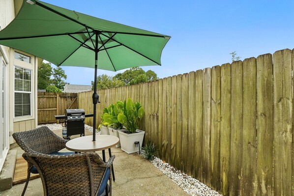 Un patio con mobiliario de mimbre, una mesa y un paraguas verde.