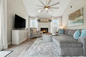A living room with a fireplace, a television, a ceiling fan, and a large painting on the wall. - Sea Horse Cove: Fully Fenced, Kid and Pet Friendly (Fort Walton Beach)