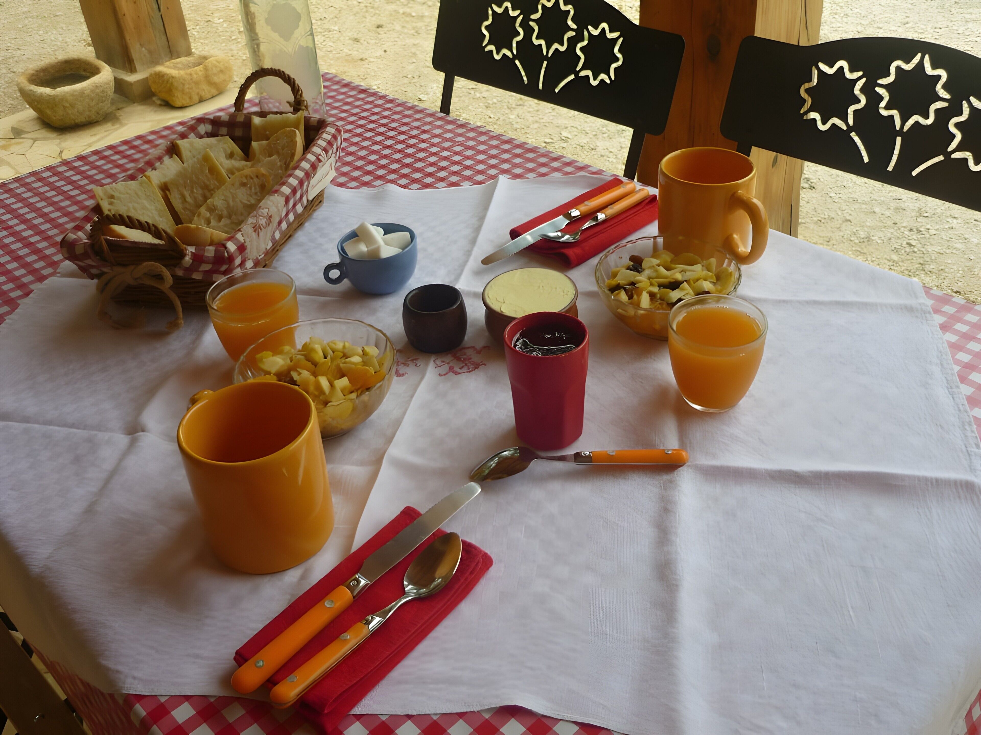 Una tavola imbandita per la colazione, con pane, frutta e bevande, una tovaglia a quadretti e sedie di legno.