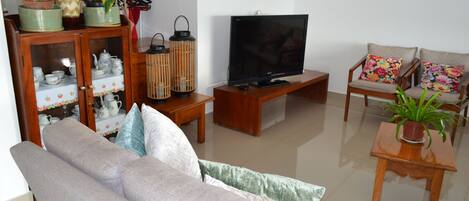 Una sala de estar con sofá, televisor, aparador de madera y plantas en macetas.