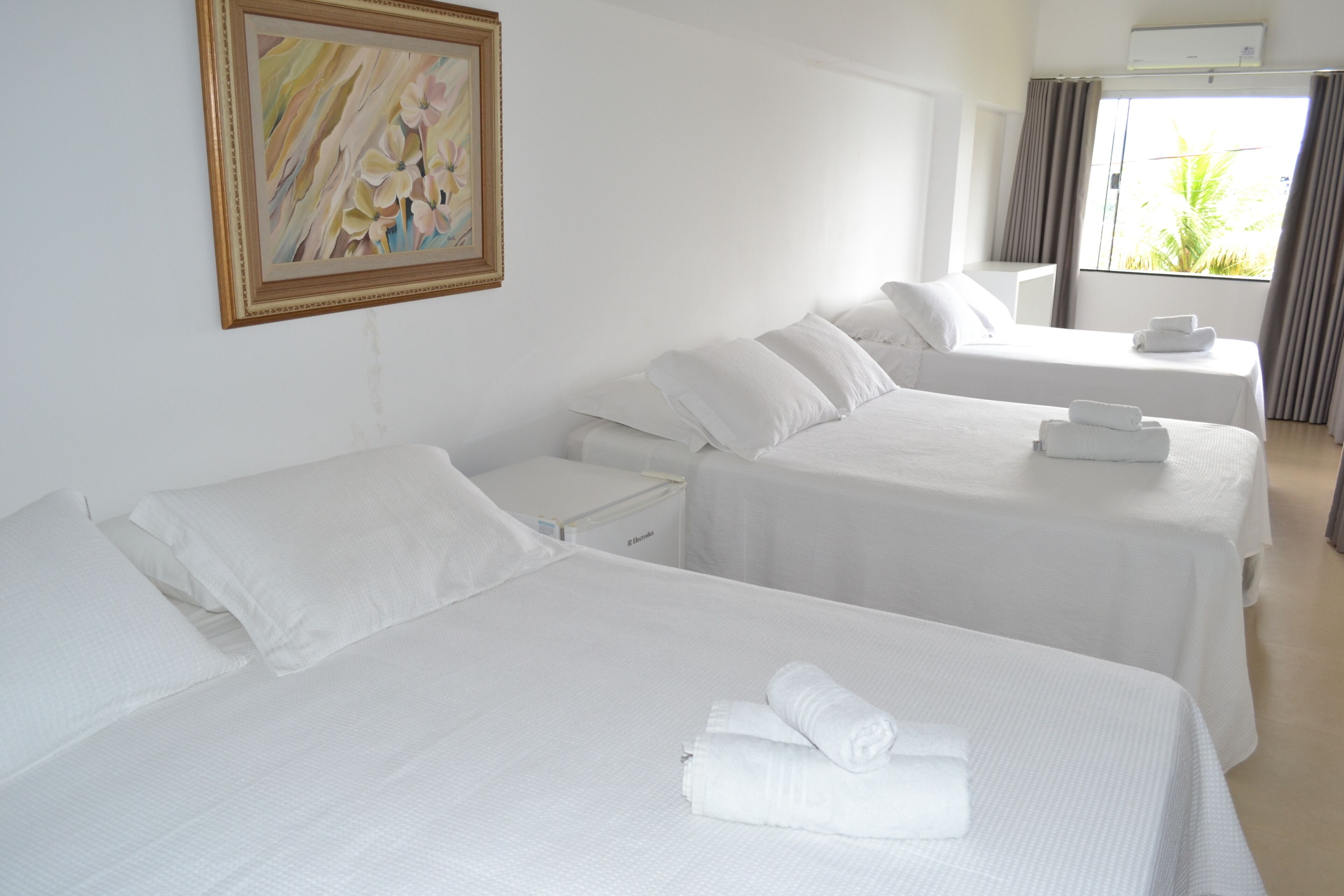 Una habitación de hotel con dos camas, un cuadro en la pared y una ventana con cortinas.