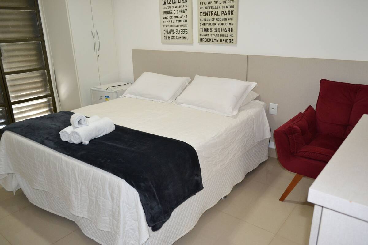 A hotel room with a bed, a red chair, and a white desk.