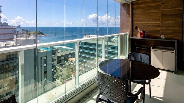 Ein Balkon mit Blick auf das Meer und die Stadtlandschaft, einem runden Tisch und einer Küchenzeile mit einer Kaffeemaschine.
