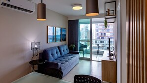 Ein modernes Wohnzimmer mit einer Couch, einem Esstisch und Stühlen. Es gibt ein großes Fenster mit Blick auf Gebäude.