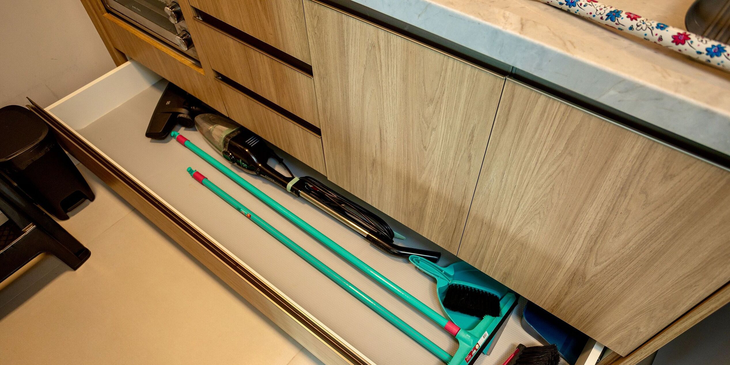 Eine Küche mit Holzschränken, einer Arbeitsplatte und verschiedenen Küchenutensilien, darunter ein Besen, ein Kehrblech und eine Sprühflasche.