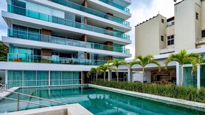 Ein modernes Hotel mit Schwimmbad, mehreren Balkonen und üppiger Bepflanzung.