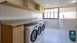 Een moderne wasruimte met ingebouwde wasmachines en drogers, een granieten aanrechtblad en een raam dat voor daglicht zorgt.