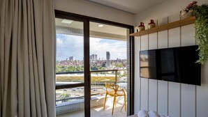 Hotelkamer met een groot raam, een flatscreen televisie aan de muur, een bed met opgerolde handdoeken, een stoel en een kleine tafel.