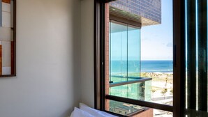 A hotel room with a large window offering a view of the ocean and a modern building. - Sea View 2Bedroom Apartment on Salvador’s Shore (Salvador)