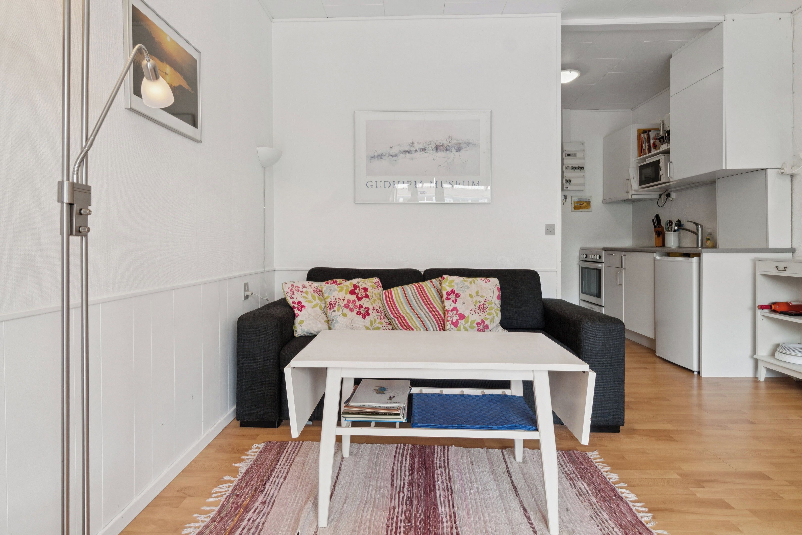 Een moderne woonkamer met een witte bank, een klein wit tafeltje en een keuken in de achtergrond.
