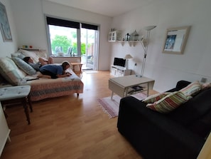 Una sala de estar con sofá, un sillón negro, una mesa de centro, televisor y una estantería.