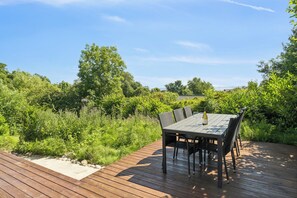 A wooden deck with a table and chairs, surrounded by lush greenery and trees. - Holiday home with spa sauna and sea view (Rønde)
