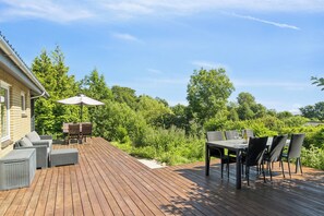 Een houten terras met buitenmeubilair, waaronder een tafel en stoelen, en een overdekte zithoek.
