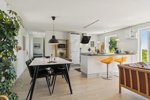 Eine moderne KĂŒche mit Kochinsel, Essbereich mit StĂŒhlen und einer Sitzecke mit Sofa.