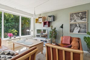 Uma sala de estar moderna com uma janela grande, uma televisão, uma mesa de jantar e um sofá.