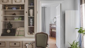 Une pièce avec un meuble en bois, un fauteuil recouvert d’un tissu vert, un mur blanc et un plancher en bois.