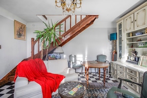 A living room with a staircase, a white sofa, a red throw, a round coffee table, and a bookshelf. - Holiday Home 'Chez Poton' with Private Terrace, Shared Garden and Wi-Fi (Le Grand-Bourg)