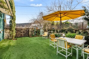A patio with a white table and yellow chairs, a yellow umbrella, and a green lawn.