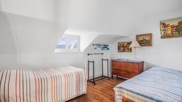 Quarto com duas camas, cómoda de madeira, candeeiro e um quadro na parede.