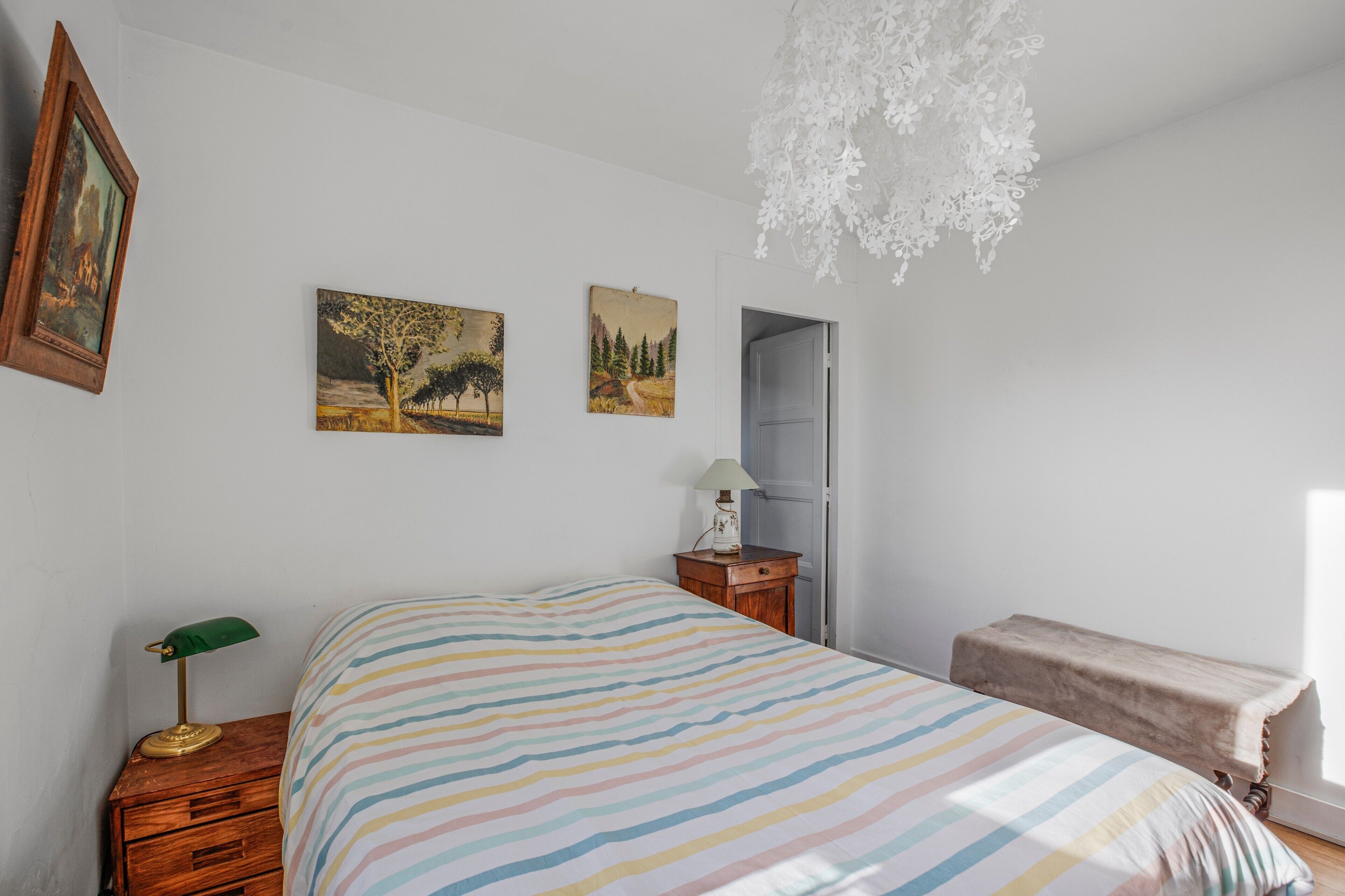 Ein Schlafzimmer mit einem Bett, einem Nachttisch, einer Lampe, einer Kommode und zwei Wandbildern.