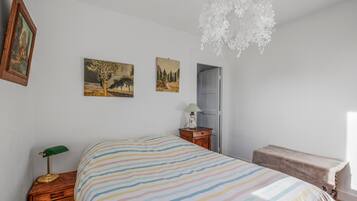 Ein Schlafzimmer mit einem Bett, einem Nachttisch, einer Lampe, einer Kommode und zwei Wandbildern.