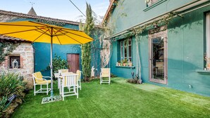 Une cour avec un parasol jaune, des chaises blanches et une pelouse verte.
