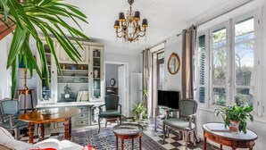 Un salon avec un sol à carreaux, un lustre, un téléviseur et une grande plante.