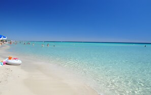 A beach with clear turquoise water, a sandy shore, and a few people swimming. - Apartment 'A Casa Di Palma - 2' with Wi-Fi and Air Conditioning (marina di pulsano)