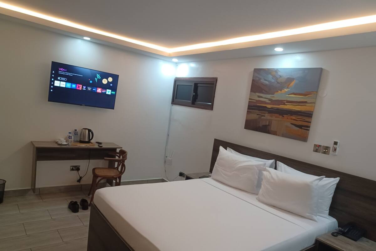 A hotel room with a bed, a desk with a chair, a TV mounted on the wall, and a painting on the wall.