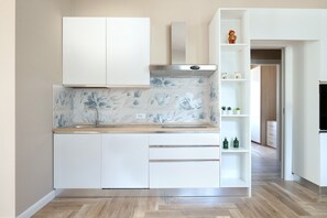 A modern kitchen with white cabinetry, a marble backsplash, and a wooden countertop.
