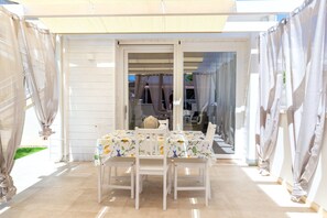 Ein Essbereich im Freien mit Tisch und Stühlen, eine überdachte Terrasse und Vorhänge.