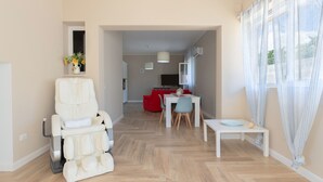 Een moderne woonkamer met een massagestoel, een eethoek met een tafel en stoelen, en een keuken op de achtergrond.
