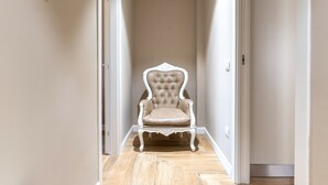 Een gang met een witte, beklede stoel, houten vloeren en witte wanden.