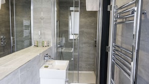 A modern bathroom with a glass-enclosed shower, a white sink, and a vanity with toiletries. - Spacious 2-Bedroom Executive Apartment – Ideal for Business Travellers (London)