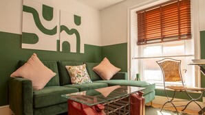 Een woonkamer met een groene bank, een glazen salontafel en een rieten fauteuil.