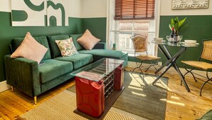Een moderne woonkamer met een groene bank, een rode salontafel en een eethoek met rieten stoelen.