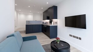 Un salon moderne avec un canapé bleu, un téléviseur à écran plat fixé au mur, et une petite table ronde sur laquelle se trouvent une télécommande et un vase à fleurs.